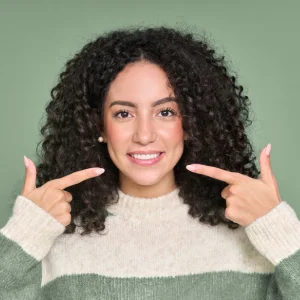 Young woman with bright smile pointing at her teeth after teeth whitening in Newark